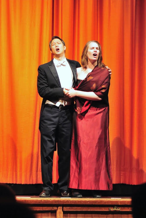 Rod Lowe in a tuxedo and Michèle in a gown, on stage, singing and over-acting