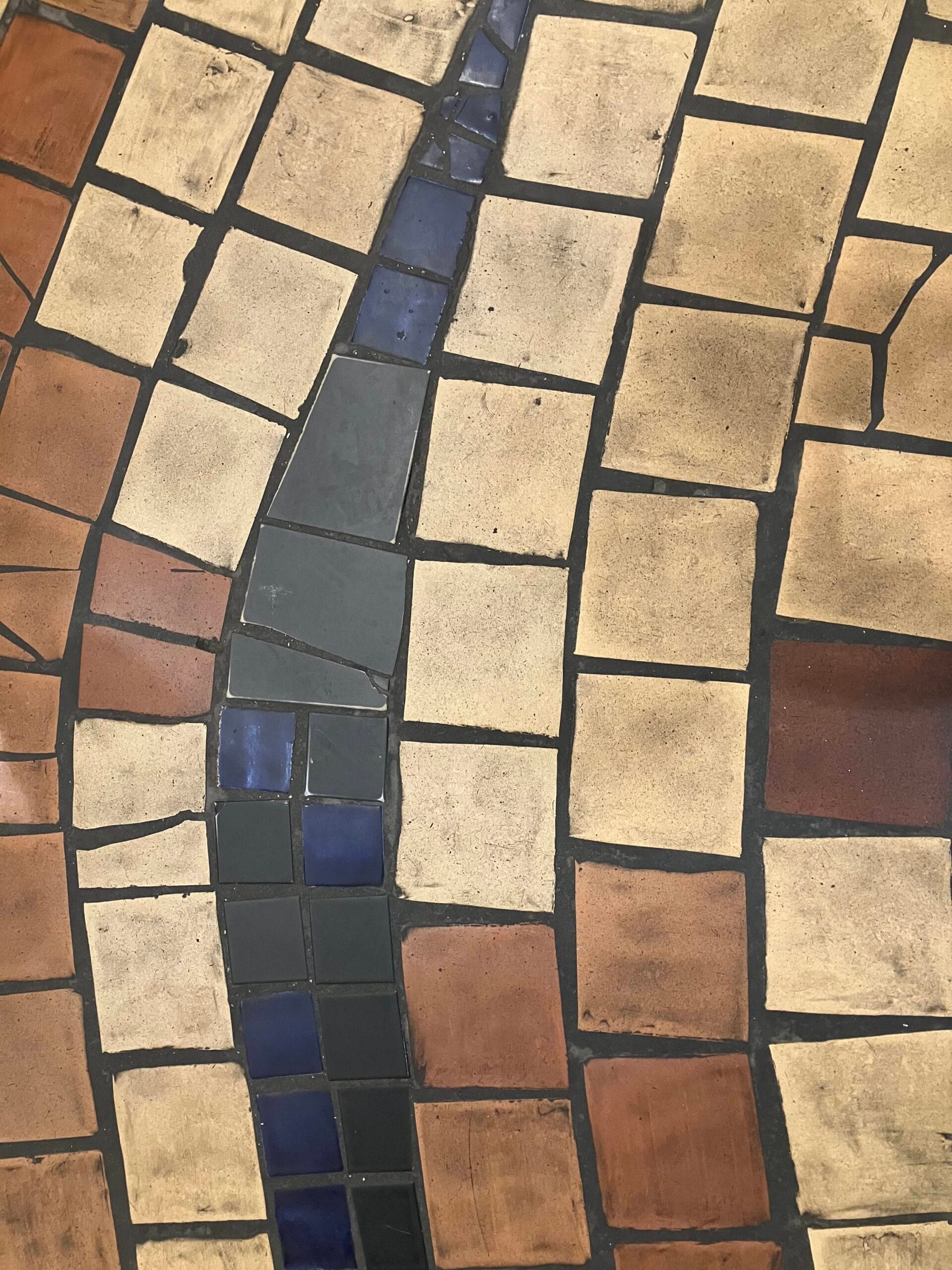 Geometric mosaic paving with beige, terracotta, and dark-blue tiles separated by black grout.